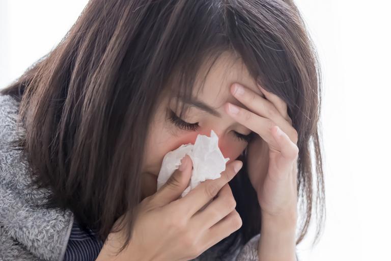 a stressed woman sneezing into a tissue